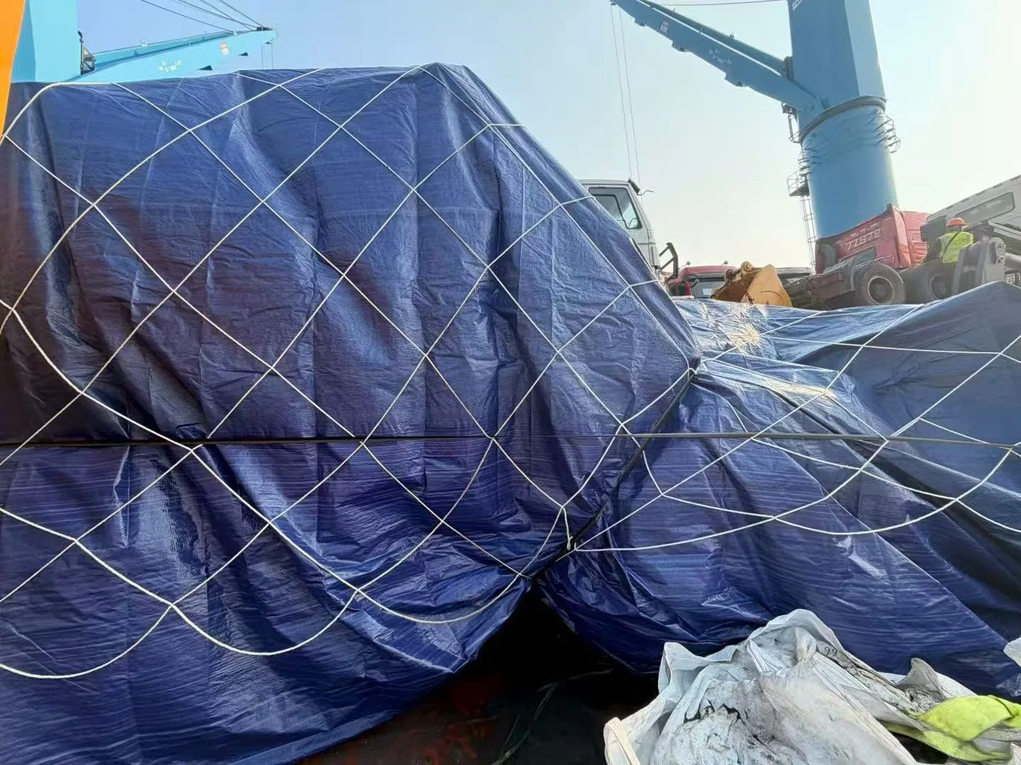 Machines covered with tarpaulin and secured with lashing nets on a break bulk vessel